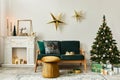 Stylish christmas living room interior with green sofa, white chimney, christmas tree and wreath, stars, gifts and decoration. Royalty Free Stock Photo