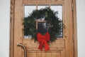 Stylish christmas rustic wreath with red bow on wooden doors at house entrance. Winter holiday decoration of modern farmhouse Royalty Free Stock Photo