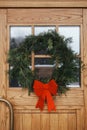 Stylish christmas rustic wreath with red bow on wooden doors at house entrance. Winter holiday decoration of modern farmhouse Royalty Free Stock Photo