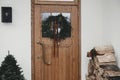 Stylish christmas rustic wreath with vintage bells and ribbon on wooden doors, fir tree and lantern on house exterior. Winter