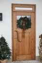 Stylish christmas rustic wreath with vintage bells and ribbon on wooden doors, fir tree and lantern on house exterior. Winter