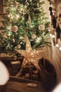 Stylish Christmas star, tree with white baubles, boho ornaments, golden lights and gifts in atmospheric evening room. Festive