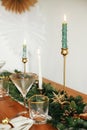 Stylish Christmas table setting. Linen napkin with bell on plate, vintage cutlery, wineglass, fir branches with golden lights,