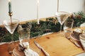 Stylish Christmas table setting. Linen napkin with bell on plate, vintage cutlery, wineglass, fir branches with golden lights,
