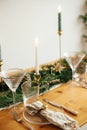 Stylish Christmas table setting. Linen napkin with bell on plate, vintage cutlery, wineglass, fir branches with golden lights,