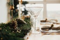 Stylish Christmas table setting. Linen napkin with bell on plate, vintage cutlery, wineglass, fir branches with golden lights,