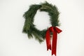 Stylish christmas wreath with red bow hanging on white wall. Merry Christmas and Happy Holidays! Simple traditional xmas wreath Royalty Free Stock Photo