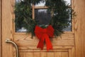 Stylish christmas wreath with red bow hanging on wooden front door at house entrance. Modern minimal farmhouse exterior decor for Royalty Free Stock Photo