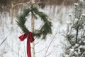 Stylish Christmas wreath on tree in snowy winter park. Simple xmas wreath with pine branches and red bow hanging outdoors. Rustic Royalty Free Stock Photo