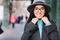 Stylish city portrait young pretty woman in grey hat, black glasses walking on street in centre. Luxury coat