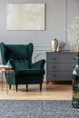 Stylish coffee table next to emerald green armchair in trendy living room interior with grey design
