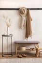 The stylish composition of cosy entryway with grey bench, coffee table, hanger and personal accessories. Beige wall. Home decor.