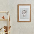 Stylish composition of cozy scandi child`s room interior with mock up poster frame, bed, plush caterpillar on balance board, toys. Royalty Free Stock Photo