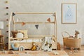 Stylish composition of cozy scandinavian child`s room interior with wooden bed, plush and wooden toys, rattan basket and textile.