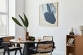 Stylish composition of dining room interior with design table, modern chairs, decoration, tropical leaf in vase, fruits, bookcase. Royalty Free Stock Photo