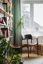 Stylish composition of home office interior with design retro chair, home library, plant, window, books, decoration