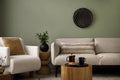 Stylish composition of living room interior with green wall, grey sofa with pillow. White armchair with brown pilow, wooden coffe