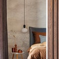 Stylish composition of modern bedroom interior. Bed, creative lamp and elegant personal accessories. Concrete wall. Brown sheeets