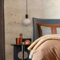 Stylish composition of modern bedroom interior. Bed, creative lamp and elegant personal accessories. Concrete wall. Brown sheeets