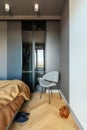 Stylish composition of modern bedroom interior. Wardrobe , grey chair and elegant personal accessories. Grey wall. Brown sheeets.