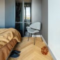 Stylish composition of modern bedroom interior. Wardrobe , grey chair and elegant personal accessories. Grey wall. Brown sheeets.