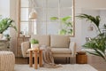 Stylish composition of modern living room with beige sofa, coffee table, pouf, plants and personal accessories. Home staging.