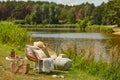 Stylish composition of outdoor garden on the lake with design rattan armchair, coffee table, plaid, pillows, drinks, elegant. Royalty Free Stock Photo