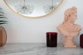 Stylish composition of pink classic sculpture with red candle glass on white marble top with copy space on white wall background