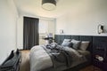 Stylish composition of small modern bedroom interior. Bed, creative lamp and elegant personal accessories. Walls with black panel.