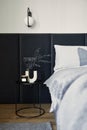 Stylish composition of small modern bedroom interior. Bed, creative lamp and elegant personal accessories. Walls with black panel.