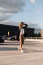Stylish cool woman in fashionable casual clothes from new collection in trendy sunglasses in white sneakers walks on asphalt on Royalty Free Stock Photo
