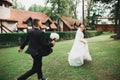Stylish couple of happy newlyweds. Bride running from groom in the park on their wedding day with bouquet Royalty Free Stock Photo
