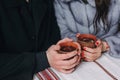 Stylish couple holding cups with hot tea in hands on wooden porch in winter snowy mountains. Happy romantic family with drinks. H Royalty Free Stock Photo