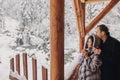 Stylish couple holding hot tea in cups and looking at winter snowy mountains from wooden porch. Happy romantic family with drinks Royalty Free Stock Photo
