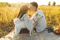 Stylish couple kissing, relaxing  in sunny light with white dog on blanket  in summer meadow. Picnic Royalty Free Stock Photo