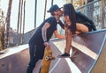 Stylish couple in love. Beautiful girl sitting on a ramp and kissing her boyfriend in the skatepark at the summertime Royalty Free Stock Photo