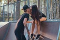 Stylish couple in love. Beautiful girl sitting on a ramp and kissing her boyfriend in the skatepark at the summertime Royalty Free Stock Photo