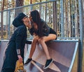 Stylish couple in love. Beautiful girl sitting on a ramp and kissing her boyfriend in the skatepark at the summertime Royalty Free Stock Photo