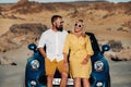 A stylish couple, a man and a woman, stand next to a blue car against the backdrop of the desert on the island of Tenerife. Royalty Free Stock Photo