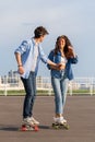 Stylish couple skateboarding together over urban skyline. Young adult man and woman on londboard Royalty Free Stock Photo