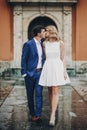 Stylish couple walking and kissing in european city street on background of old architecture. Fashionable bride and groom in love Royalty Free Stock Photo