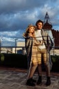 Stylish couple wrapped in blanket stand at the balcony at sunset, handsome man hug gorgeous woman, loving husband enjoy