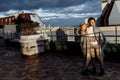 Stylish couple wrapped in blanket stand at the balcony at sunset, handsome man hug gorgeous woman, loving husband enjoy