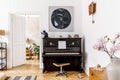 Stylish and cozy interior of living room with black piano, furniture, plant, wooden clock, lamp, mock up painitngs, carpet. Royalty Free Stock Photo