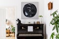 Stylish and cozy interior of living room with black piano, furniture, plant, wooden clock, lamp, mock up painitngs, carpet.