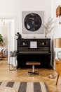 Stylish and cozy interior of living room with black piano, furniture, plant, wooden clock, lamp, mock up painitngs, decoration. Royalty Free Stock Photo