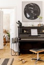 Stylish and cozy interior of living room with black piano, furniture, plant, wooden clock, lamp, mock up painitngs, decoration. Royalty Free Stock Photo