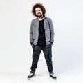 Stylish curly guy with a beard dressed in a black t-shirt, gray jacket, khaki pants and sneakers poses in the studio on Royalty Free Stock Photo