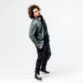 Stylish curly guy with a beard dressed in a black t-shirt, gray jacket, khaki pants and sneakers poses in the studio on Royalty Free Stock Photo