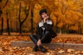 Stylish cute young woman in fashionable warm clothes in leather trendy boots in a sits posing in a park on the ground among orange